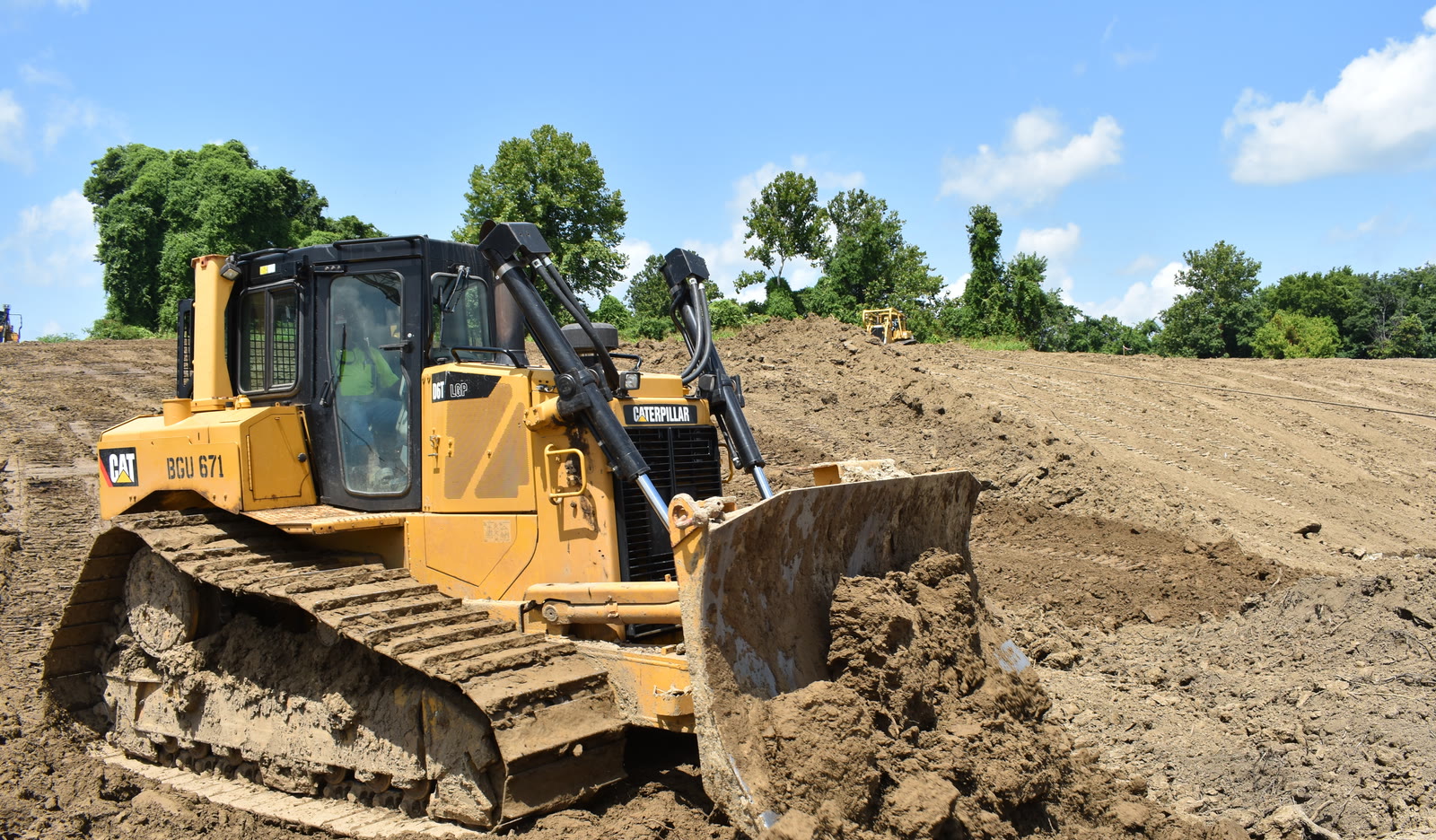Bouteur Caterpillar D6T sur chenilles vu de trois quarts avant, la lame pleine de terre, sur un chantier de terrassement