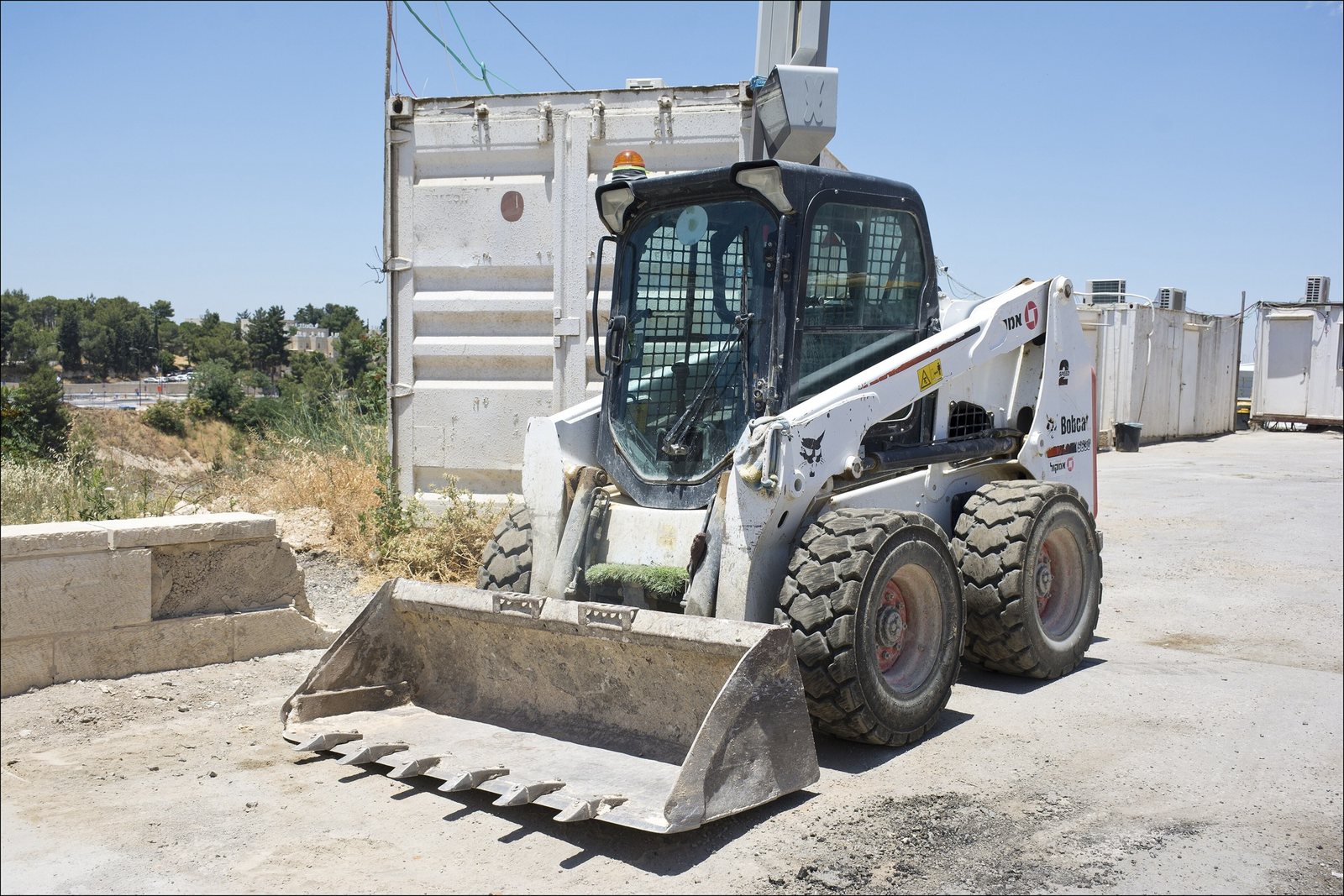 Chargeur compact Bobcat S630 sur pneus, godet au sol, stationné sur un terrain de chantier