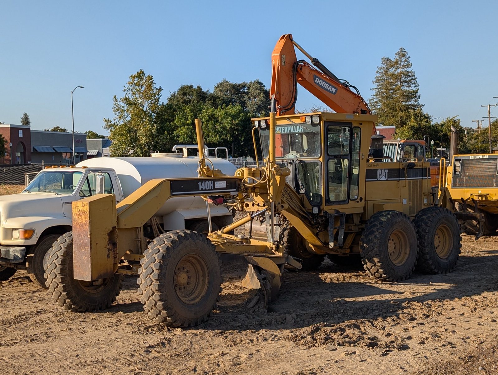 Niveleuse Caterpillar 140H sur un chantier de terrassement, lame abaissée, d’autres machines en arrière-plan