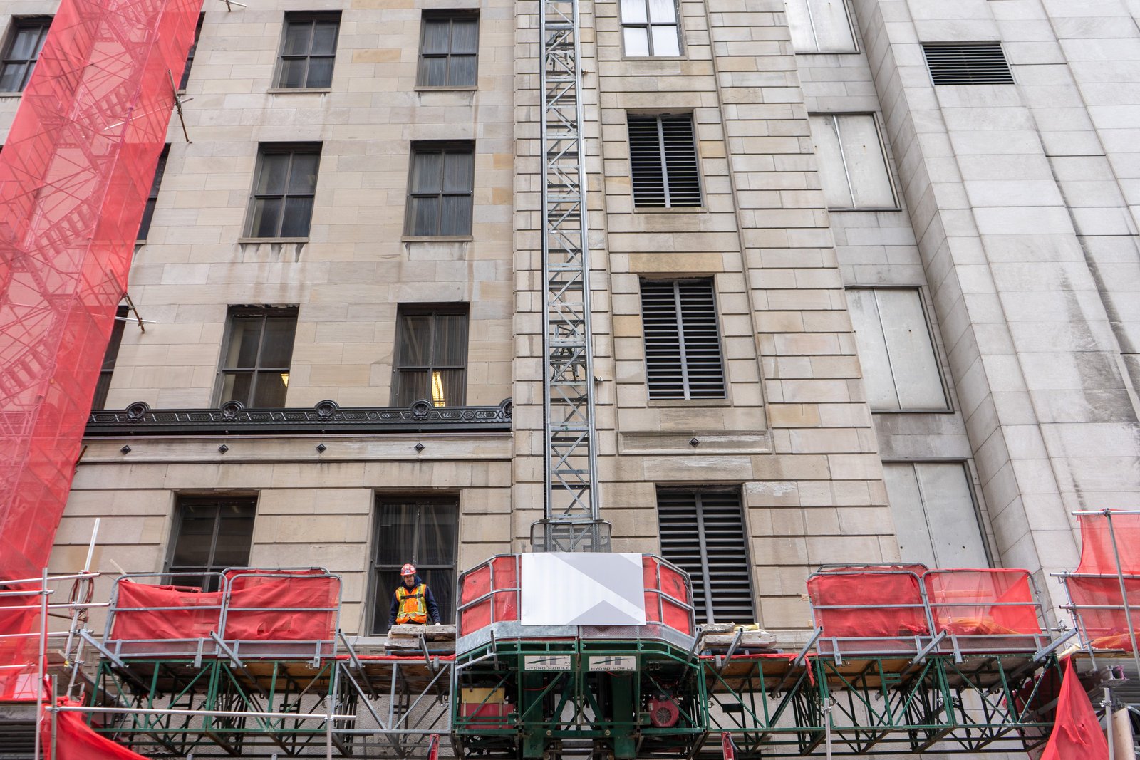 Plateforme de travail sur mât installée contre la façade en pierre d'un immeuble de Montréal, avec son mât vertical et un travailleur en dossard sur le plancher