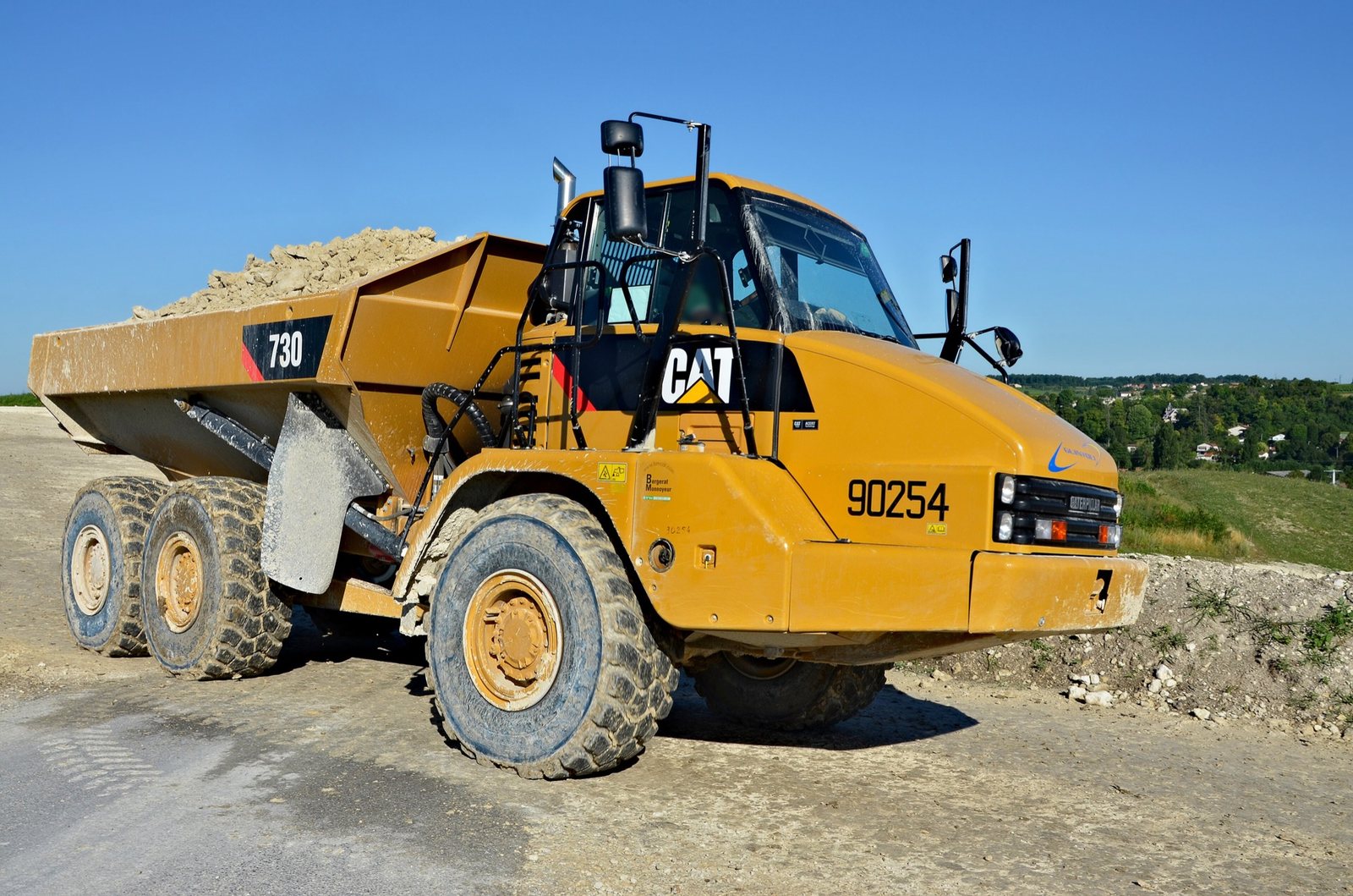Tombereau articulé Caterpillar 730 chargé de pierre sur une piste de chantier