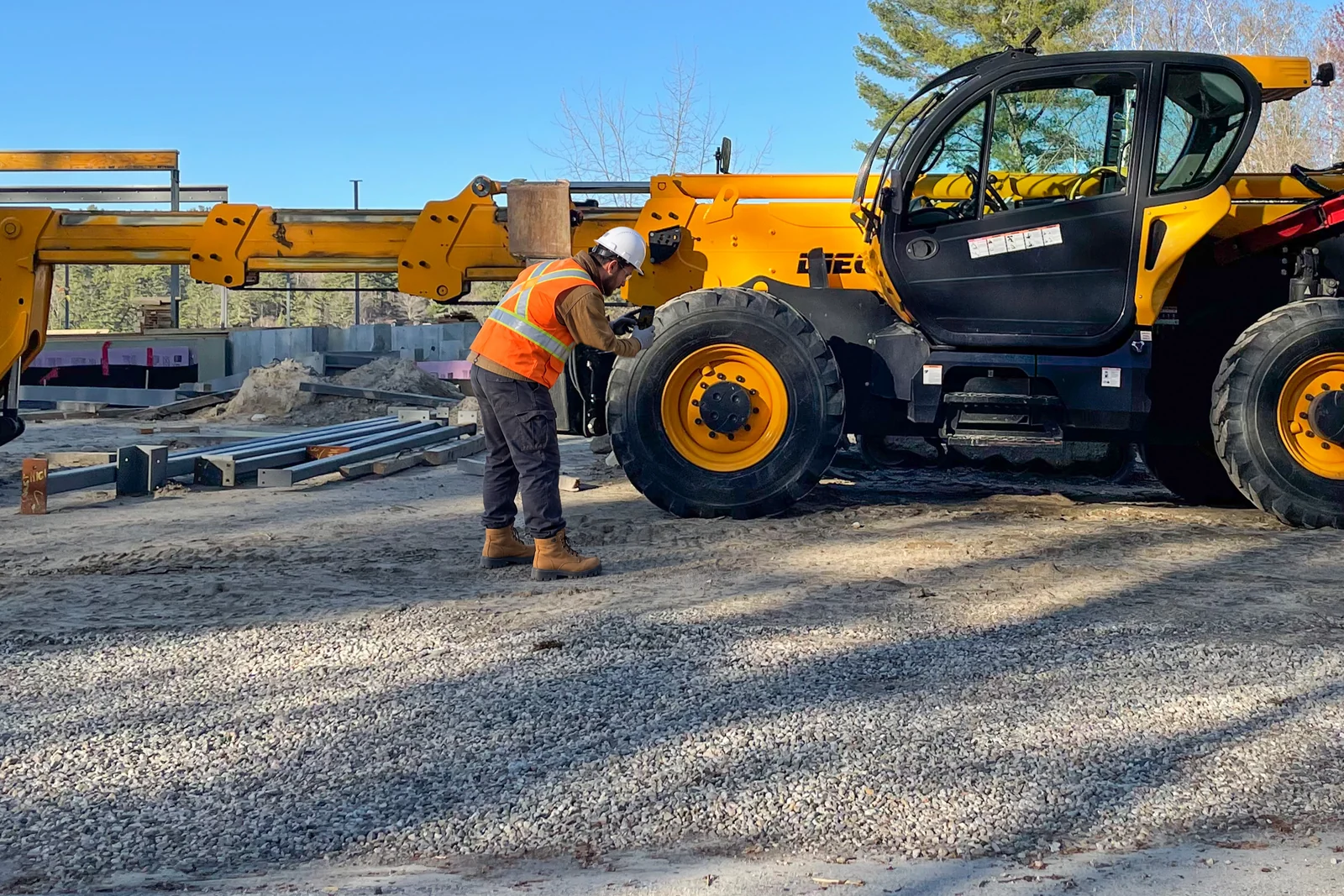 Opérateur qui inspecte la roue d’un chariot télescopique sur un chantier